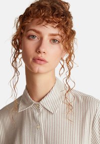 Camicia con colletto a righe verticali sottili in crema e bordeaux. Tessuto morbido, chiusura con bottoni, colletto visibile, tessuto ben stirato.