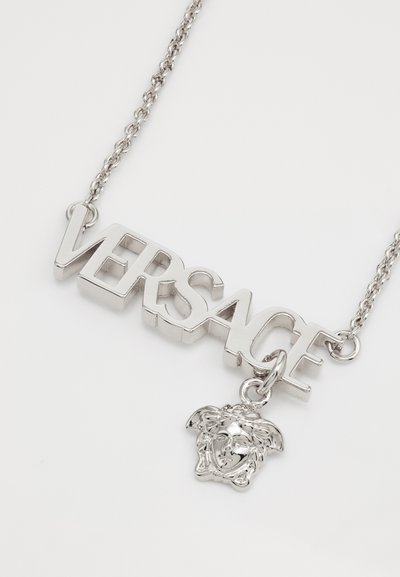 Strieborný reťazový náhrdelník s výrazným nápisom "VERSACE" v tučnom písme a príveskom Medúzy, s lesklým povrchom a 3D dizajnovými prvkami.