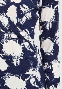 Blommönstrad tyg med marinblå och vita färger; texturerat ribbat material; har en omslagdesign och långa ärmar.