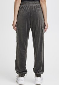 Grijze velours cargobroek met een elastische tailleband, zijzakken en boorden bij de enkel, gecombineerd met witte sneakers.