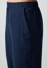Pantalons en lin bleu marine avec une coupe décontractée, dotés de poches latérales et de plis à l'avant pour un look structuré. Ceinture élastique.