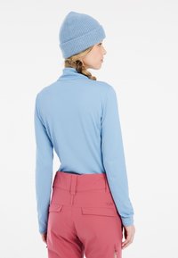Camicia a maniche lunghe azzurra con una texture morbida, abbinata a pantaloni rosa a vita alta con tasche e una cintura liscia. Berretto azzurro lavorato a maglia.