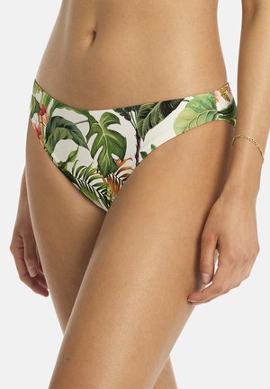 Kobieta nosząca dół bikini z zielonym tropikalnym wzorem liści i kwiatów, pokazująca brzuch i górną część ud na jednolitym tle.