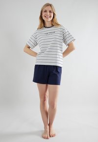 Gestreepte T-shirt met korte mouwen in wit en marineblauw, gecombineerd met marineblauwe shorts. Het materiaal lijkt zacht, met een relaxte pasvorm en een minimalistisch ontwerp.