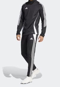 Svart idrottsoverall bestående av en långärmad topp med kvart dragkedja, vita detaljer och matchande byxor med tre vita ränder.