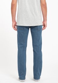 Light blue denim jeans with a straight leg design feature stitching accents and back pockets. Worn with a gray t-shirt and white sneakers.