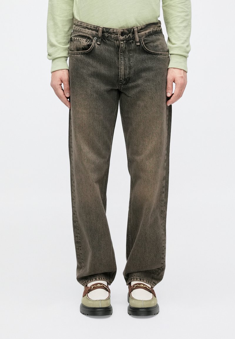Dark, faded denim jeans with a straight leg cut; features five pockets, belt loops, and a zip fly. Worn with shoes that have a dual color accent.