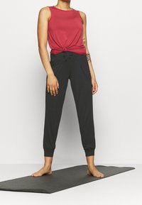 Rød ærmeløs top med knudedetalje, parret med sorte tapered joggerbukser med elastiske manchetter og forlommer; blødt, åndbart stof.