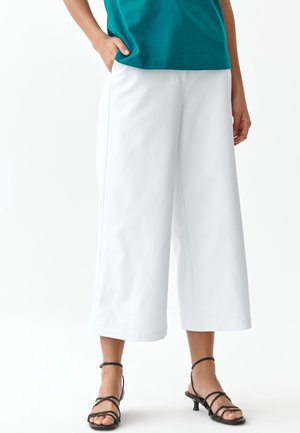 Culotte bianche realizzate in tessuto leggero, con una vestibilità ampia e gamba dritta, abbinate a sandali neri con cinturini.