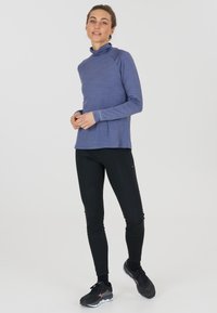 Langärmliges, blaues Sportoberteil mit Stehkragen, kombiniert mit schwarzen, enganliegenden Leggings und schwarzen Sportschuhen mit dezenten Akzenten.