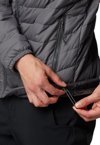Grau gestepptes Jacket mit Reißverschluss und elastischen Bündchen. Hände, die den Kordelzug am Saum verstellen. Glattes, leichtes Material.