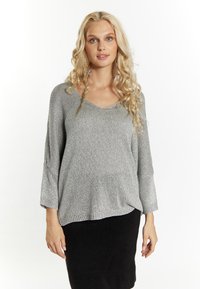 Maglione grigio lavorato a maglia con scollo a V, vestibilità morbida e maniche a tre quarti, abbinato a una gonna nera. Tessuto soffice e dettagli lucidi.