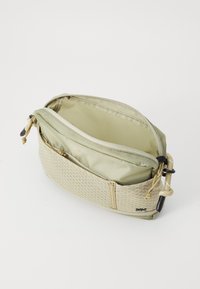 Borsa leggera di colore verde oliva in tessuto con un motivo texturizzato, due scomparti con zip e una piccola tasca laterale con hardware resistente.
