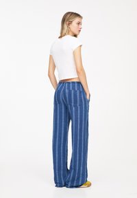Blå stribede vidde-bukser med en afslappet pasform, designet med et tekstureret stof og to baglommer. Sammen med en tætsiddende hvid crop top.