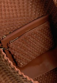 Geweven bruin leren schoudertas met een ritsvak aan de binnenkant in dezelfde textuur, een gladde afwerking en dubbele handvatten.