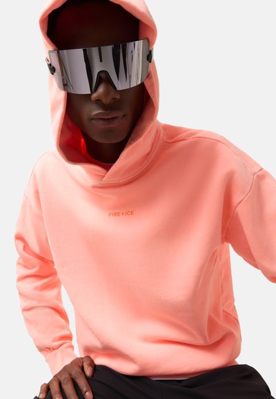 Bluza z kapturem w jaskrawym różowym kolorze o miękkiej strukturze, z małym pomarańczowym logo "FIRE + ICE". Model nosi lustrzane okulary przeciwsłoneczne.