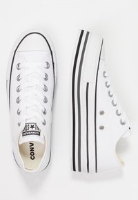 Baskets montantes blanches avec des rayures noires sur la semelle, dotées de lacets et d'une étiquette de marque visible sur la languette.