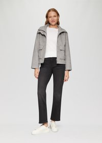 Grijze jas met een capuchon, twee voorzakken en een rits, gedragen over een witte trui en zwarte spijkerbroek, aangevuld met witte sneakers.