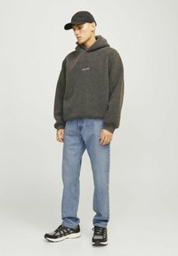 Sudadera de forro polar en gris oscuro con un bolsillo frontal y logo negro, combinada con jeans de color azul claro y zapatillas deportivas negras.