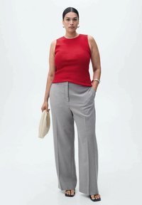 Red sleeveless top with a fitted design paired with light grey wide-leg trousers, accessorized with a woven beige clutch and simple sandals.
