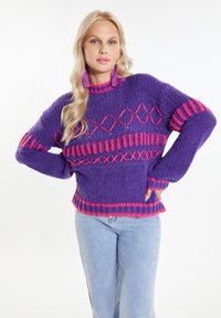 Fioletowy sweter z dzianiny z geometrycznymi różowymi wzorami, prążkowaną teksturą i luźnym krojem. Połączony z jasnoniebieskimi dżinsami.