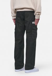 Baggy, donkergroene cargobroek met een textuurafwerking, voorzien van zijzakken, achterzakken en een klein merkje op de achterkant.