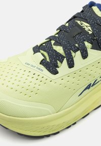 Světl zelená sportovní bota s texturovaným svrškem, černými tkaničkami a polstrovanou podrážkou. Vyniká potiskem 'ZŮSTAŇ VENKU' poblíž tkaniček.