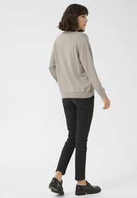 Hellgrauer Pullover mit langen Ärmeln und rundem Ausschnitt, kombiniert mit schwarzen Slim-Fit-Hosen und glänzenden schwarzen Schuhen. Einfacher, strukturiert gewebter Stoff.