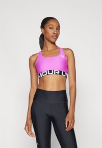 Sostén deportivo rosa con banda negra con el texto "ARMOUR UN", combinado con leggings negros de tiro alto. Tela suave, diseño ajustado.