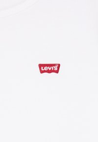 Valge puuvillane t-särk, millel on vasakus rinnas punane tikitud Levi'si logo, esitades klassikalise ümmarguse kaeluse disaini.