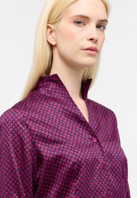 Camicia fucsia in satin con motivo a onde. Caratterizzata da un colletto a punta e chiusura con bottoni, che mette in mostra una texture liscia e lucida.