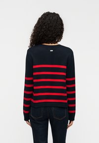 Μπλε ναυτικό πουλόβερ με κόκκινες οριζόντιες ρίγες, με ριμπ ύφανση στο λαιμό και στα μανίκια, και μικρή λεπτομέρεια λογότυπου στο πίσω μέρος.