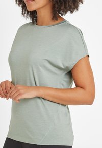 Light green athletic top with short sleeves, round neckline, smooth texture, and side seams providing a fitted silhouette.