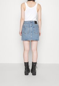 Denimkjol i ljusblått med en figurnära midja, två bakfickor och rå kant, kombinerad med svarta snörade kängor.