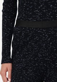 Langsleeve top in donkerblauwe geribbelde stof met verspreide lichtblauwe spikkels. Beschikt over een zwarte elastische tailleband voor een stevige pasvorm.