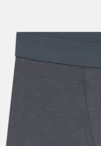 Mørkegrå elastisk talje og stofdetalje af nærbillede af herreundertøj med synlige sting på lys baggrund.