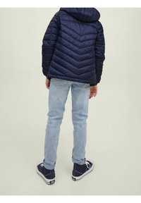 Námořnická pufová bunda s kapucí, s šikmým prošíváním. Světle modré džíny a tmavé tenisky s bílými akcenty doplňují celkový vzhled.