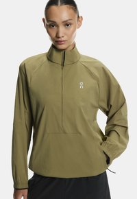 Könnyű olíva zöld pulóverdzseki magas gallérral, fél cipzárral elöl és rugalmas mandzsettákkal. Kicsi fehér logó található a mellkason.