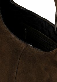 Hnědá semišová kabelka se zipovým uzávěrem, charakterizovaná měkkou texturou a prostorným vnitřkem. Podšívka je černá s malou vnitřní kapsou.