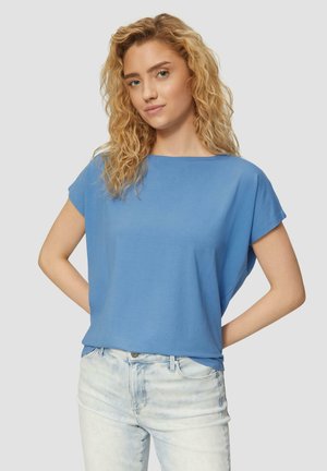 Top azzurro a maniche corte in tessuto morbido con vestibilità rilassata, caratterizzato da un ampio scollo e una texture liscia, abbinato a jeans in denim chiaro.