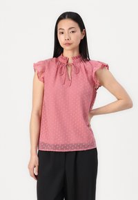 Blusa rosa a pois con maniche a volant, scollatura a occhiello e una texture morbida e leggera. L'orlo inferiore è dritto e leggermente trasparente.