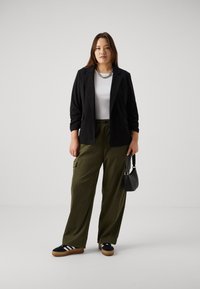 Černý blazer, bílý přiléhavý top, volné olivově zelené cargo kalhoty, černé tenisky s bílými pruhy a malá černá kabelka.