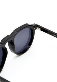 Schwarze Sonnenbrille mit geometrischem Rahmen, dunklen Gläsern und glänzender Oberfläche. Verfügt über Metallbeschläge an den Scharnieren.