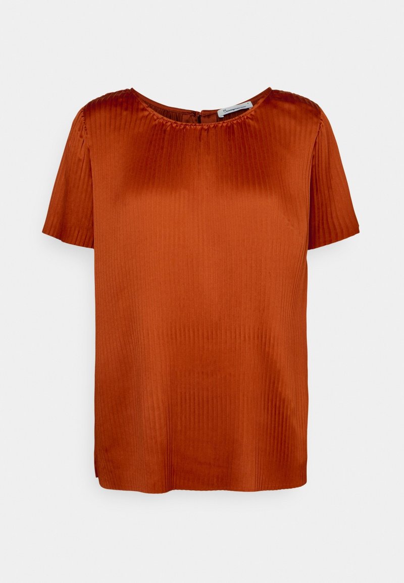 Blouse manches courtes couleur rouille-orange avec une texture subtile à côtes verticales, encolure ronde, et fermeture par boutons au dos.