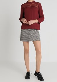 Burgunderblus med en genomskinlig spetspanel, tillsammans med en svart och vit rutmönstrad minikjol. Svarta snörskor fulländar outfiten.