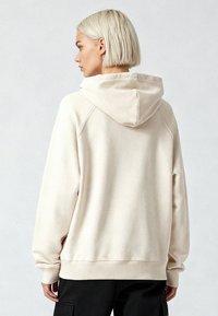 Felpa con cappuccio beige dalla vestibilità rilassata, maniche lunghe e polsini a costine. Tessuto morbido con una texture liscia, con dettaglio in giogaia sulla schiena.