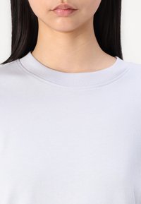 Lichtgrijs katoenen t-shirt met een ronde halslijn, korte mouwen en een gladde textuur; heeft subtiele stiksels langs de kraag.