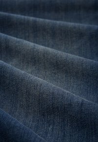 Sötétkék árnyalatú denim anyag, texturált felülettel, hajtott rétegekkel, amelyek a súlyát és szerkezetét hangsúlyozzák.