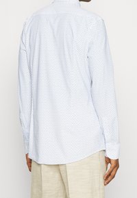 Lange mouwen shirt in lichtblauw met kleine donkerblauwe driehoekige patronen. Knopen bij de manchetten en een klassieke kraag. Glad, lichtgewicht stof.
