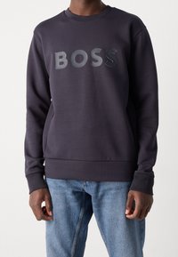 Mörkblå sweatshirt tillverkad av mjukt material har en stor, matt "BOSS"-logotyp på framsidan, rund hals och ribbade muddar och nederkant.